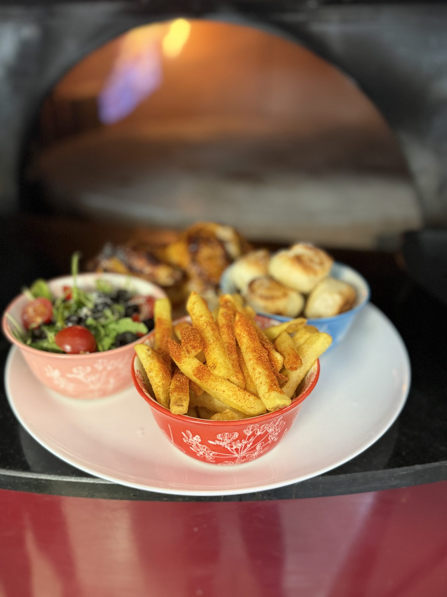 Plate of fries, salad and dough balls in front of our glowing wood-fired oven