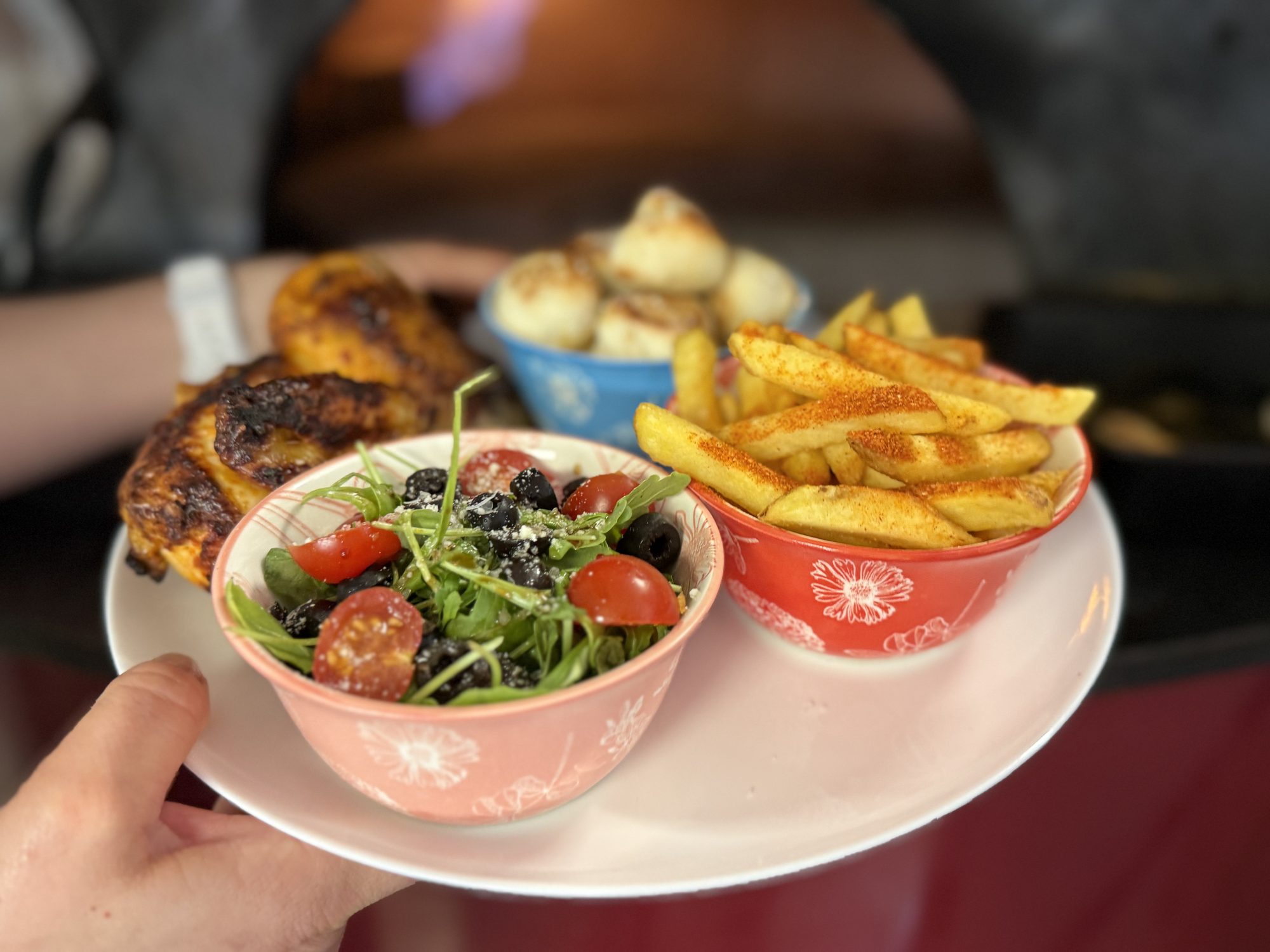 Half chicken with rocket salad and dough balls held in front of the wood-fired oven