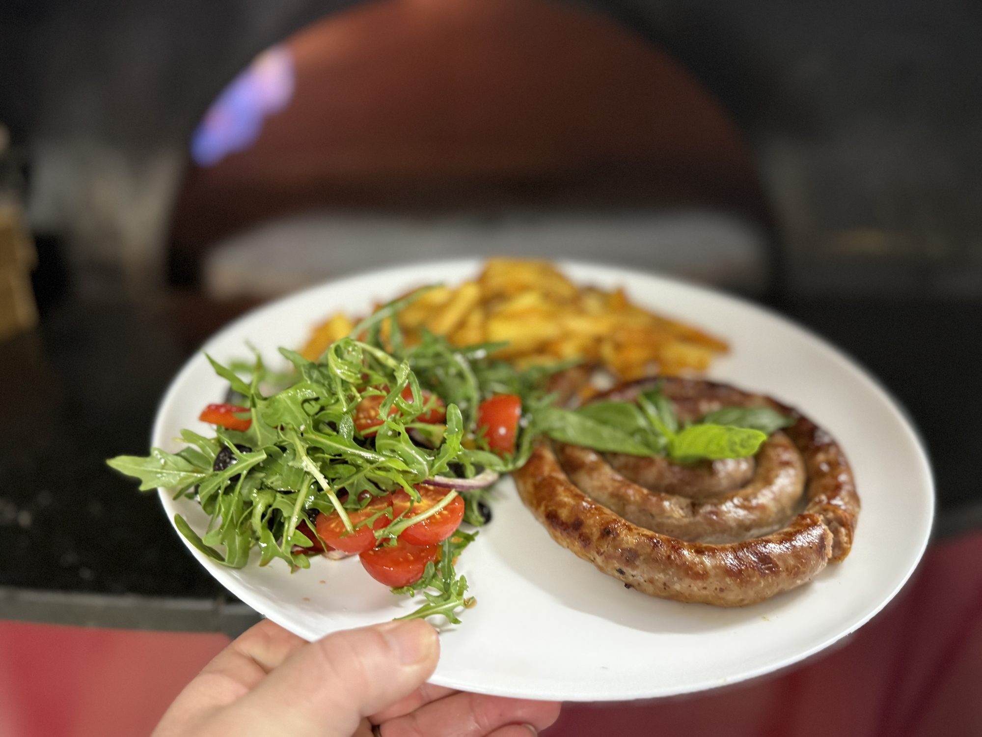Coiled Italian sausage with rocket salad and seasoned fries